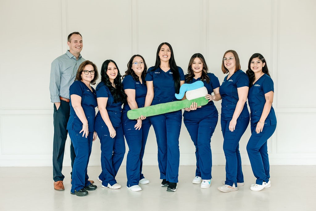 The Allen Dentistry team standing together, two of them holding an oversized toothbrush